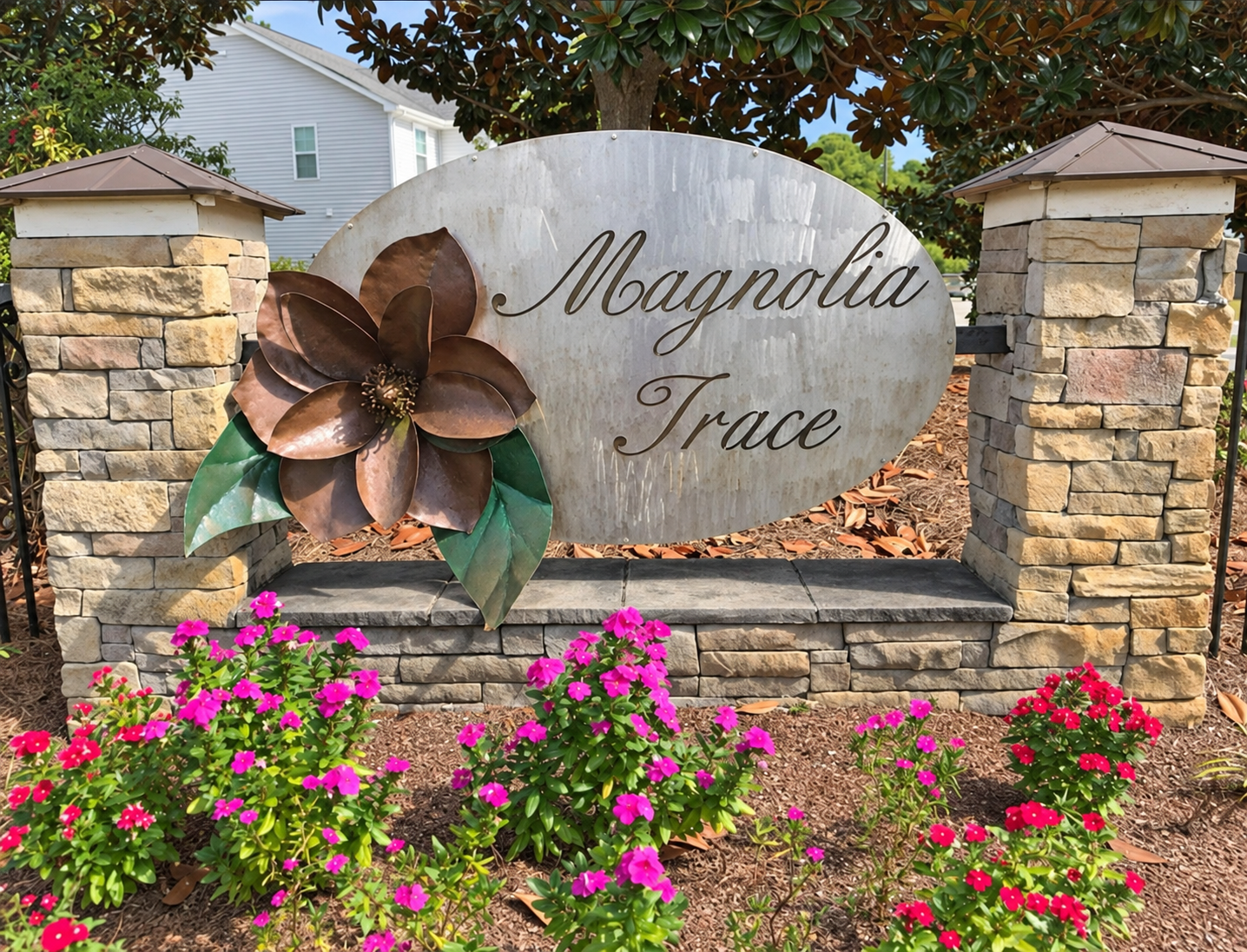 Magnolia Trace entrance sign between stone pillars, surrounded by pink flowers